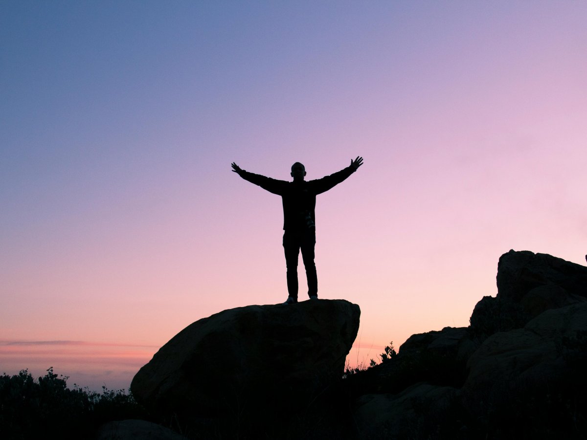 Realizing His Dreams A black silhouette of a man with arms outstretched with a sunset in the background.